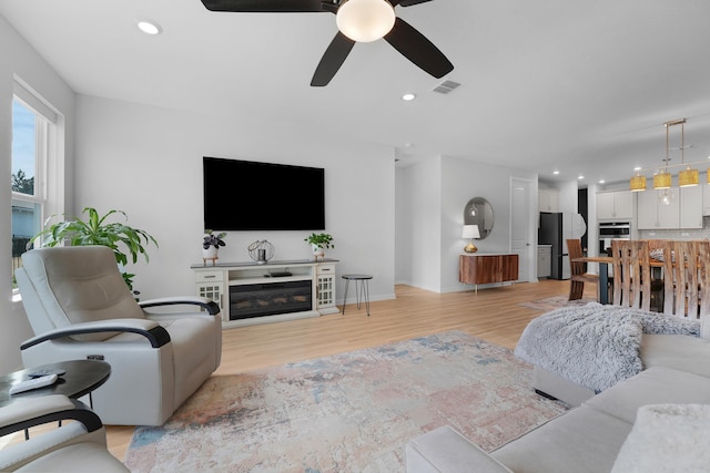 living area with recessed lighting, visible vents, light wood-style floors, a glass covered fireplace, and ceiling fan