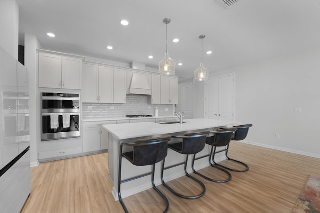 kitchen featuring a sink, gas cooktop, light countertops, double oven, and an island with sink