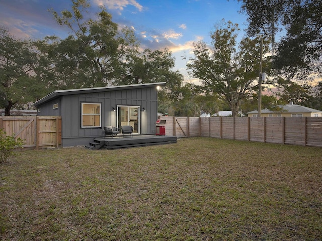 back of property at dusk featuring a fenced backyard, a gate, a deck, a yard, and board and batten siding