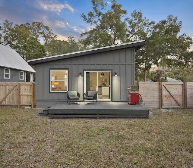 back of house at dusk featuring a gate, fence, board and batten siding, and a wooden deck