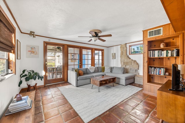 living room featuring baseboards, visible vents, ceiling fan, a textured ceiling, and crown molding