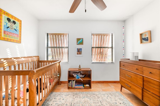 bedroom with light tile patterned floors, a nursery area, baseboards, and ceiling fan