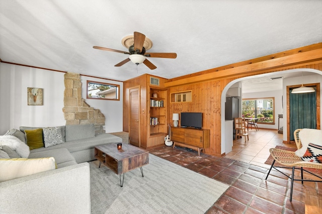 living area featuring visible vents, arched walkways, wood walls, and a ceiling fan