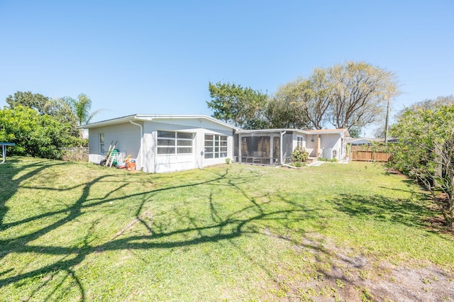 back of property featuring fence, a yard, and a sunroom