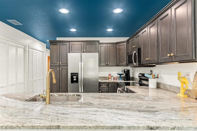 kitchen with stainless steel appliances, dark brown cabinets, sink, and light stone counters