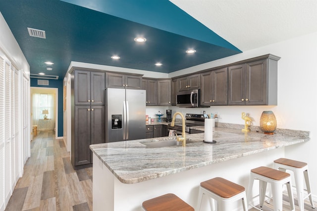 kitchen with light hardwood / wood-style flooring, appliances with stainless steel finishes, light stone counters, a kitchen bar, and kitchen peninsula