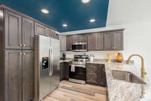 kitchen with sink, dark brown cabinets, light wood-type flooring, stainless steel appliances, and light stone countertops