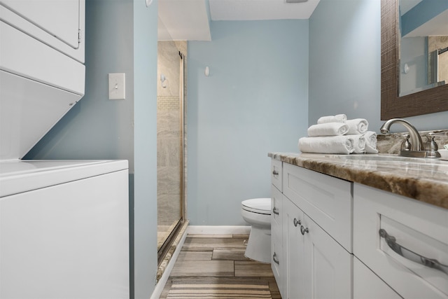 bathroom with vanity, wood-type flooring, stacked washer / dryer, toilet, and a shower with shower door