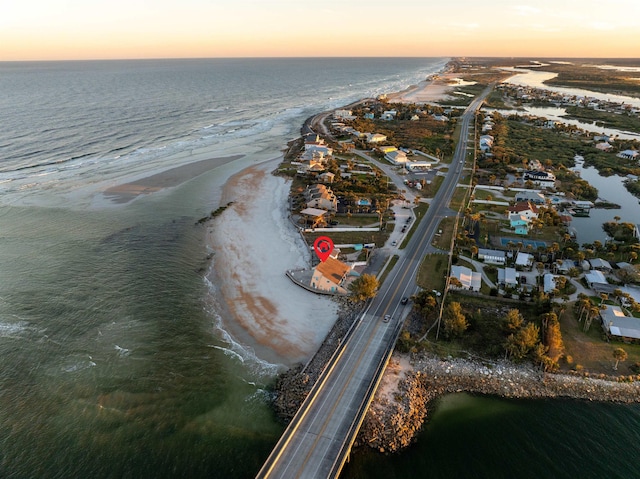 aerial view at dusk featuring a water view and a beach view