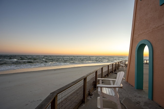 balcony at dusk featuring a water view and a view of the beach