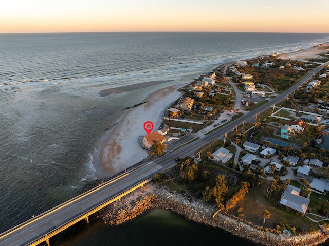 aerial view at dusk with a water view and a beach view