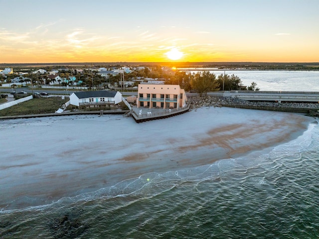 aerial view at dusk featuring a water view and a view of the beach