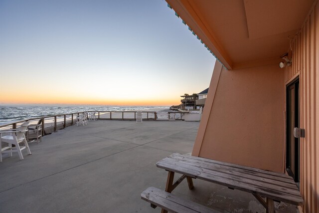 patio terrace at dusk featuring a water view and a view of the beach