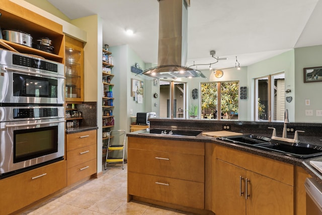 kitchen with light tile patterned floors, stainless steel appliances, a sink, brown cabinetry, and island exhaust hood