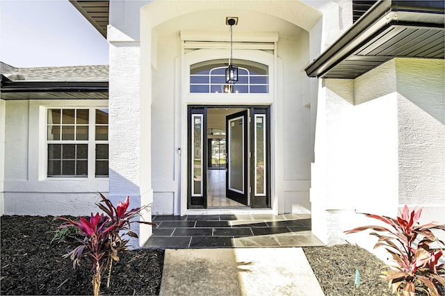 doorway to property featuring roof with shingles and stucco siding