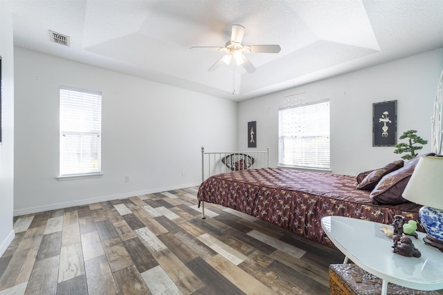 bedroom with multiple windows, a textured ceiling, dark hardwood / wood-style flooring, and a raised ceiling