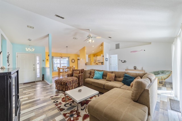 living room featuring ceiling fan with notable chandelier, light hardwood / wood-style floors, a textured ceiling, and lofted ceiling