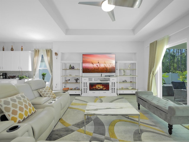 living room featuring built in shelves, a tray ceiling, and ceiling fan