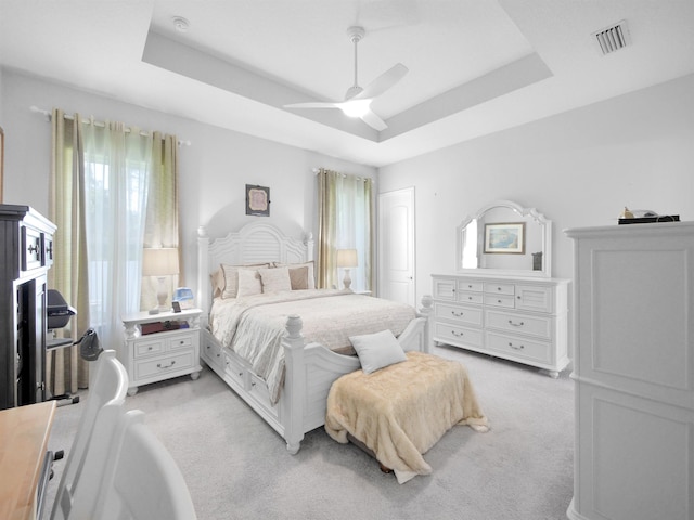 bedroom featuring ceiling fan, light carpet, and a tray ceiling