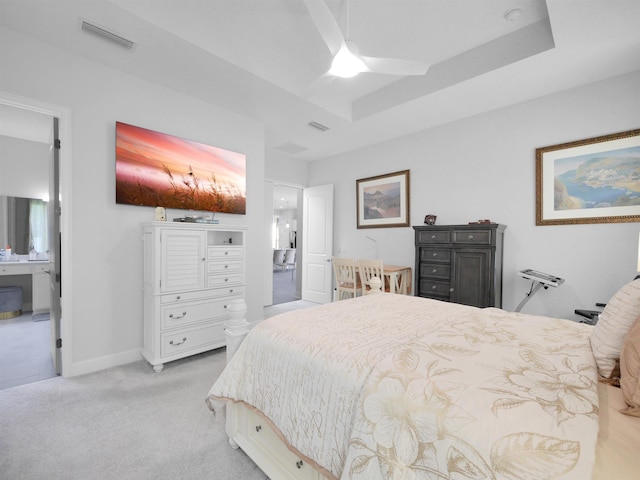 bedroom featuring ensuite bathroom, a raised ceiling, ceiling fan, and light colored carpet