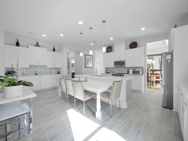 kitchen with a center island with sink, hanging light fixtures, tasteful backsplash, white cabinetry, and stainless steel appliances