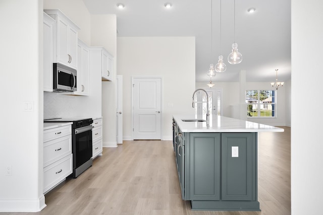 kitchen featuring white cabinetry, sink, stainless steel appliances, pendant lighting, and a kitchen island with sink