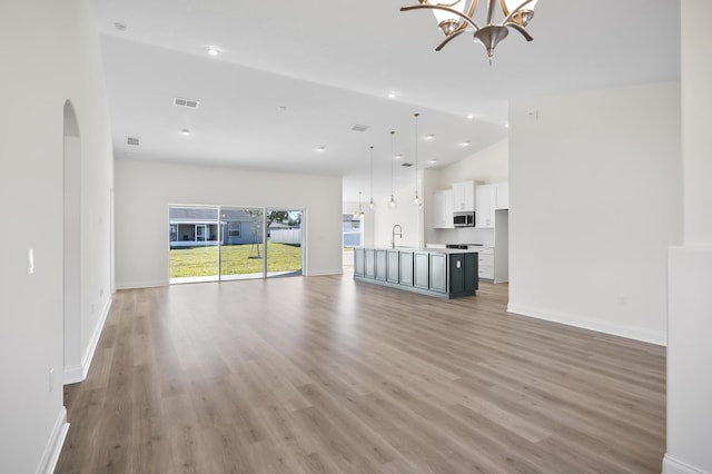 unfurnished living room featuring sink, high vaulted ceiling, a chandelier, and light wood-type flooring