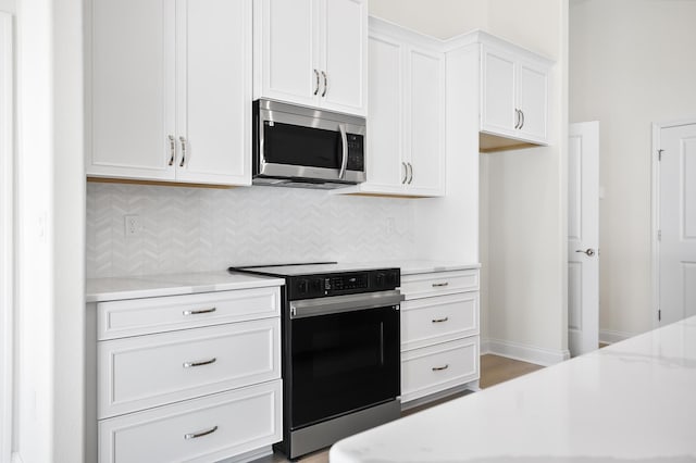 kitchen with tasteful backsplash, light stone counters, white cabinets, and appliances with stainless steel finishes