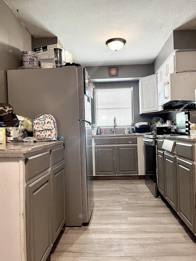 kitchen with a sink, stainless steel appliances, a textured ceiling, and light wood-style floors