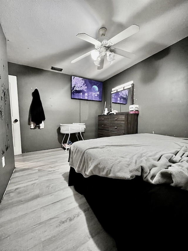 bedroom with ceiling fan, visible vents, a textured ceiling, and wood finished floors