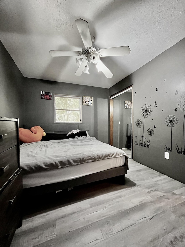 bedroom with a ceiling fan, a closet, light wood-type flooring, and a textured ceiling