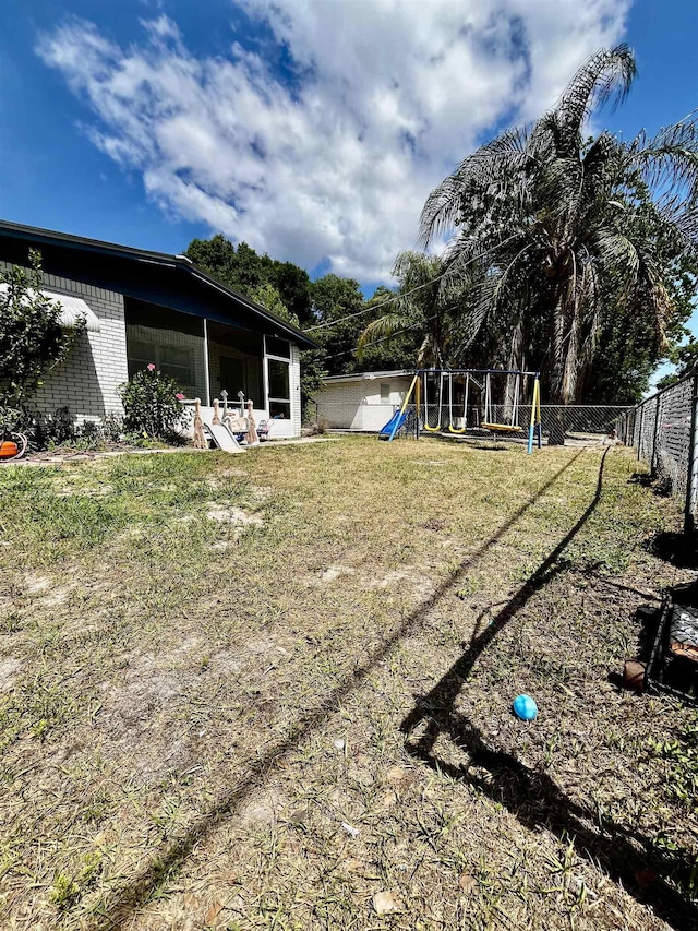view of yard featuring a sunroom, a playground, and fence