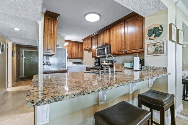 4670 A1A S Unit 1309, Saint Augustine, FL 32080 - kitchen featuring a peninsula, light stone countertops, stainless steel appliances, a sink, and washer and dryer