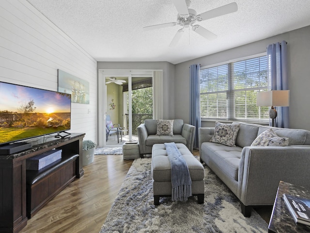 living room with wood walls, wood finished floors, a textured ceiling, and ceiling fan