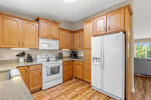 kitchen featuring light stone counters, light brown cabinetry, and white appliances