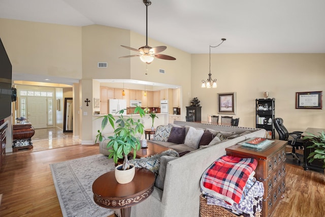 living area featuring high vaulted ceiling, ceiling fan with notable chandelier, visible vents, and wood finished floors