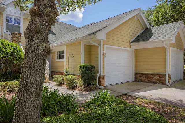 view of front of house with a garage, stone siding, a shingled roof, and driveway