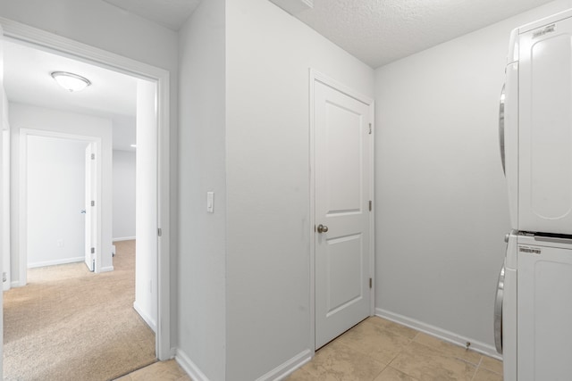 laundry area featuring light carpet, laundry area, baseboards, stacked washer / dryer, and a textured ceiling