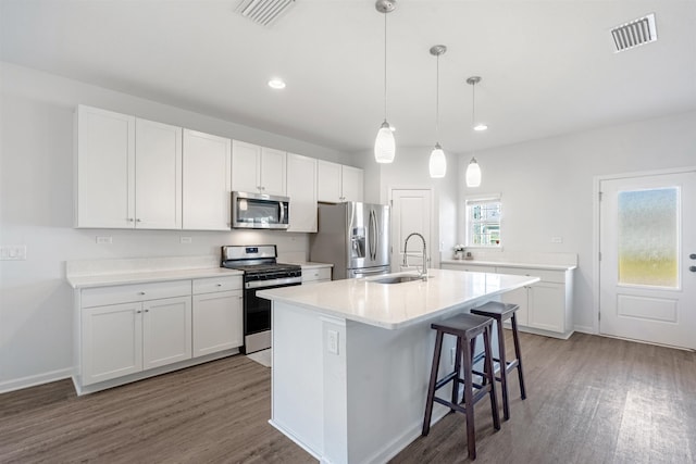 kitchen with a kitchen island with sink, white cabinets, sink, hanging light fixtures, and stainless steel appliances