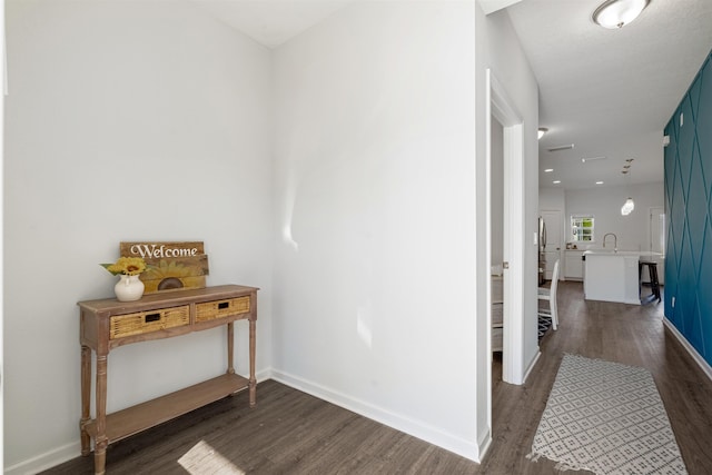 hall with dark wood-style flooring, a sink, and baseboards