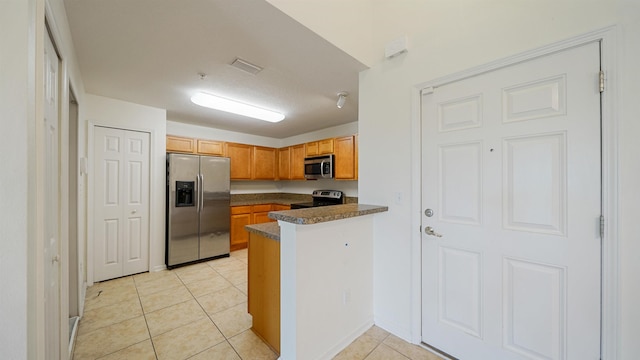 2384 Golden Lake Loop, Saint Augustine, FL 32084 - kitchen featuring stainless steel appliances, dark countertops, light tile patterned flooring, a peninsula, and brown cabinets