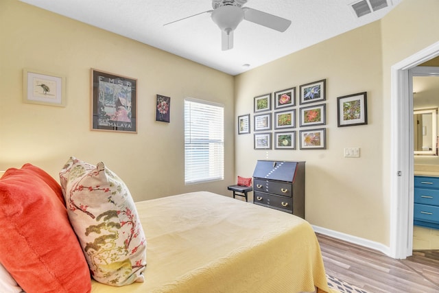 bedroom featuring visible vents, a ceiling fan, ensuite bath, wood finished floors, and baseboards