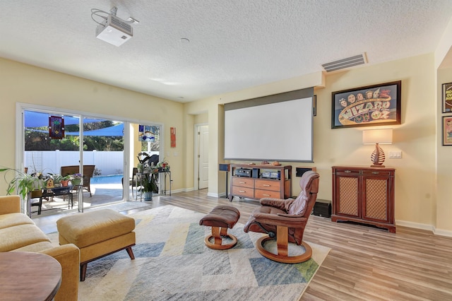 living area featuring a textured ceiling, light wood finished floors, visible vents, and baseboards