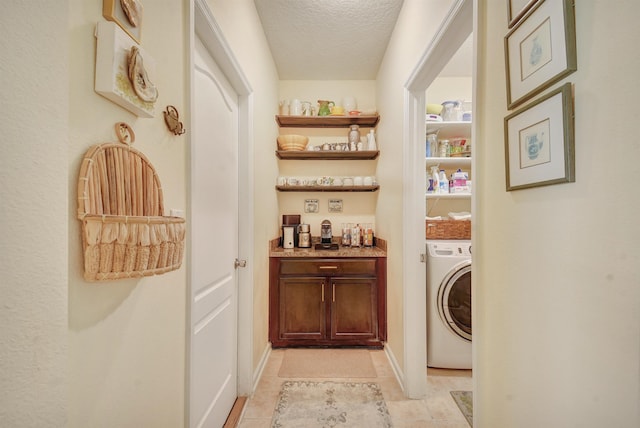 clothes washing area with washer / dryer, laundry area, light tile patterned flooring, and a textured ceiling