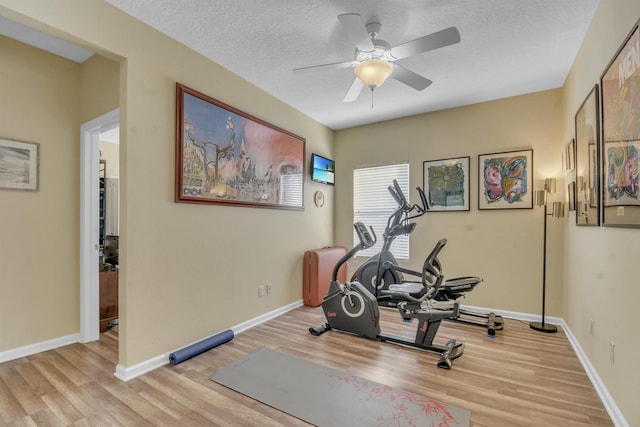 workout area with light wood-style floors, ceiling fan, baseboards, and a textured ceiling