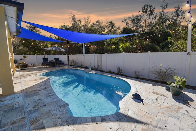 pool at dusk with a patio area, a fenced backyard, and a fenced in pool