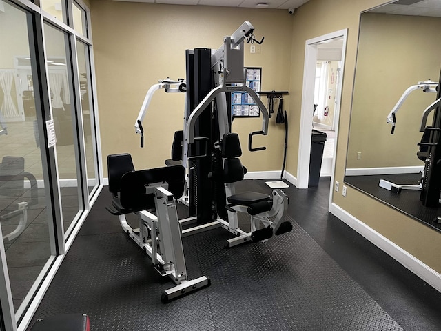 exercise room featuring a paneled ceiling and baseboards