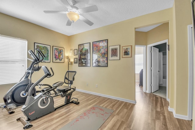 exercise room with a textured ceiling, a ceiling fan, light wood-style flooring, and baseboards