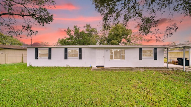 back house at dusk with a lawn and a carport