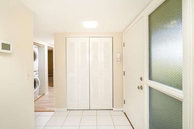 hallway with light tile patterned floors, baseboards, and stacked washing maching and dryer